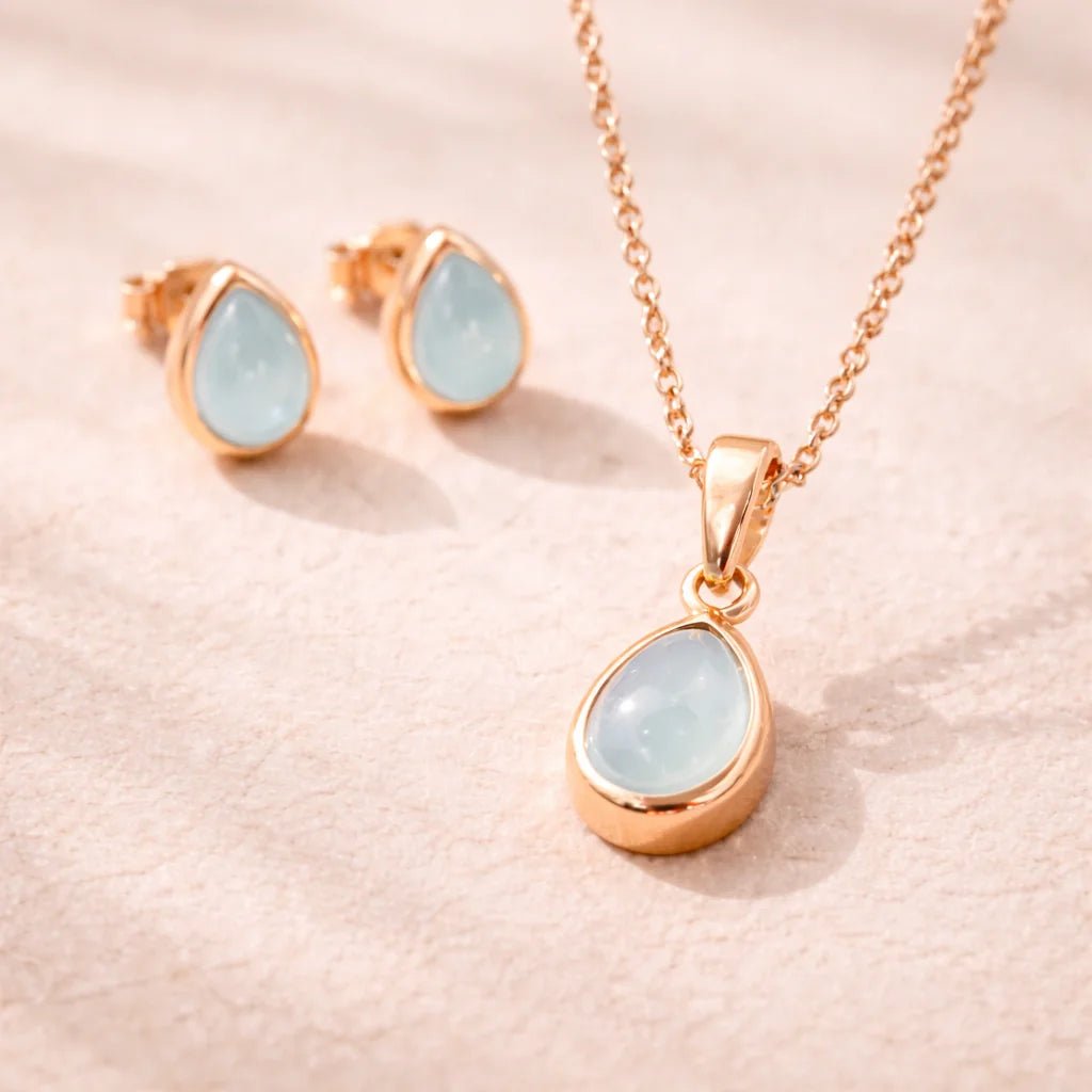 Rose Gold Jewellery set with pear drop-shaped pendant and earrings with natural bezel set aquamarine gemstones on a soft pink background