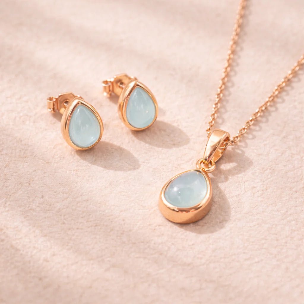 Rose Gold Jewellery set with pear drop-shaped pendant and earrings with natural bezel set aquamarine gemstones on a soft pink background