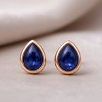 Pair of rose gold earrings with blue gemstones on a light background
