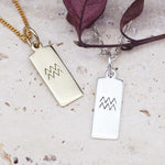 Gold and silver pendant necklaces with zodiac symbols on a textured surface.