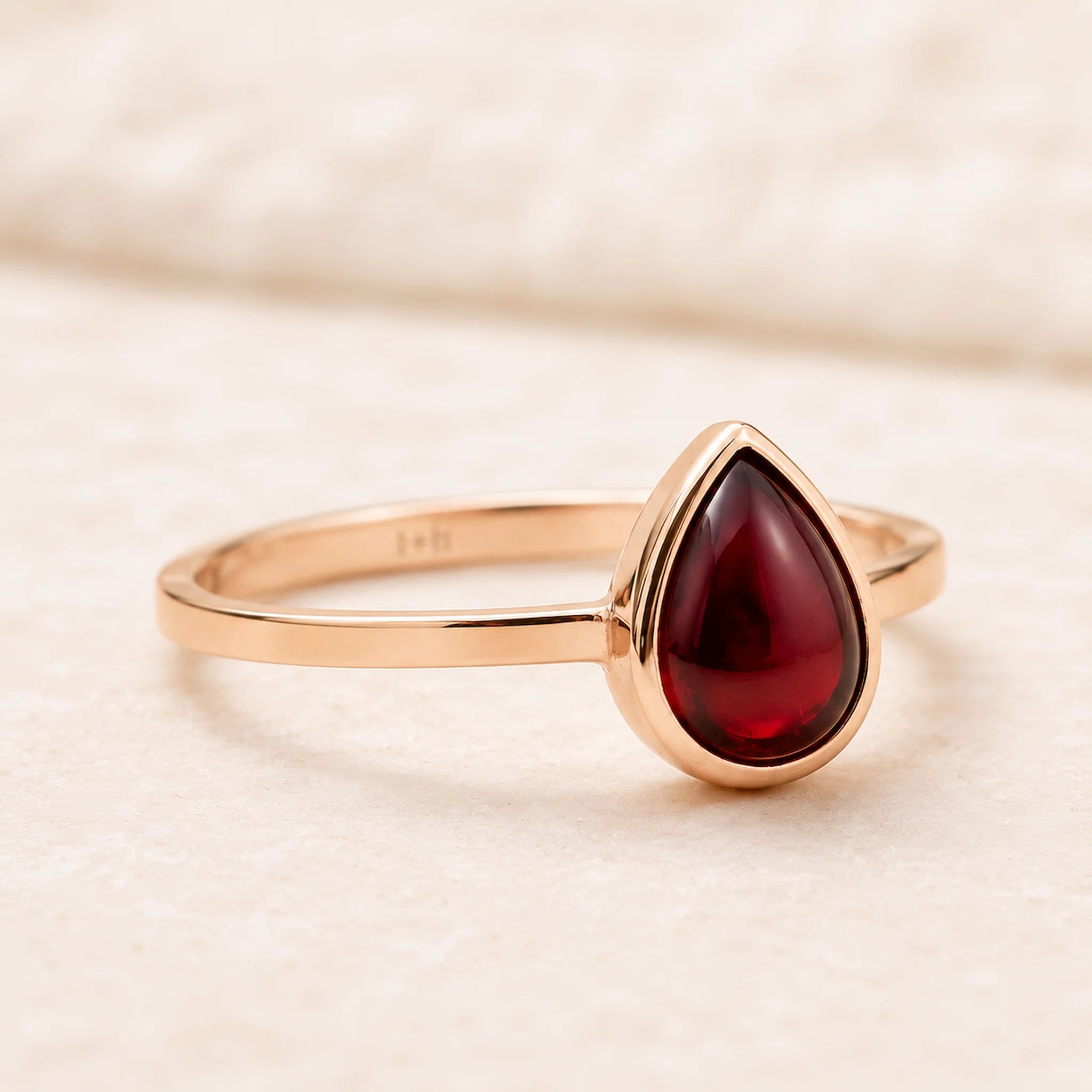 Rose Gold ring with a red teardrop-shaped january birthstone natural garnet gemstone on a beige background