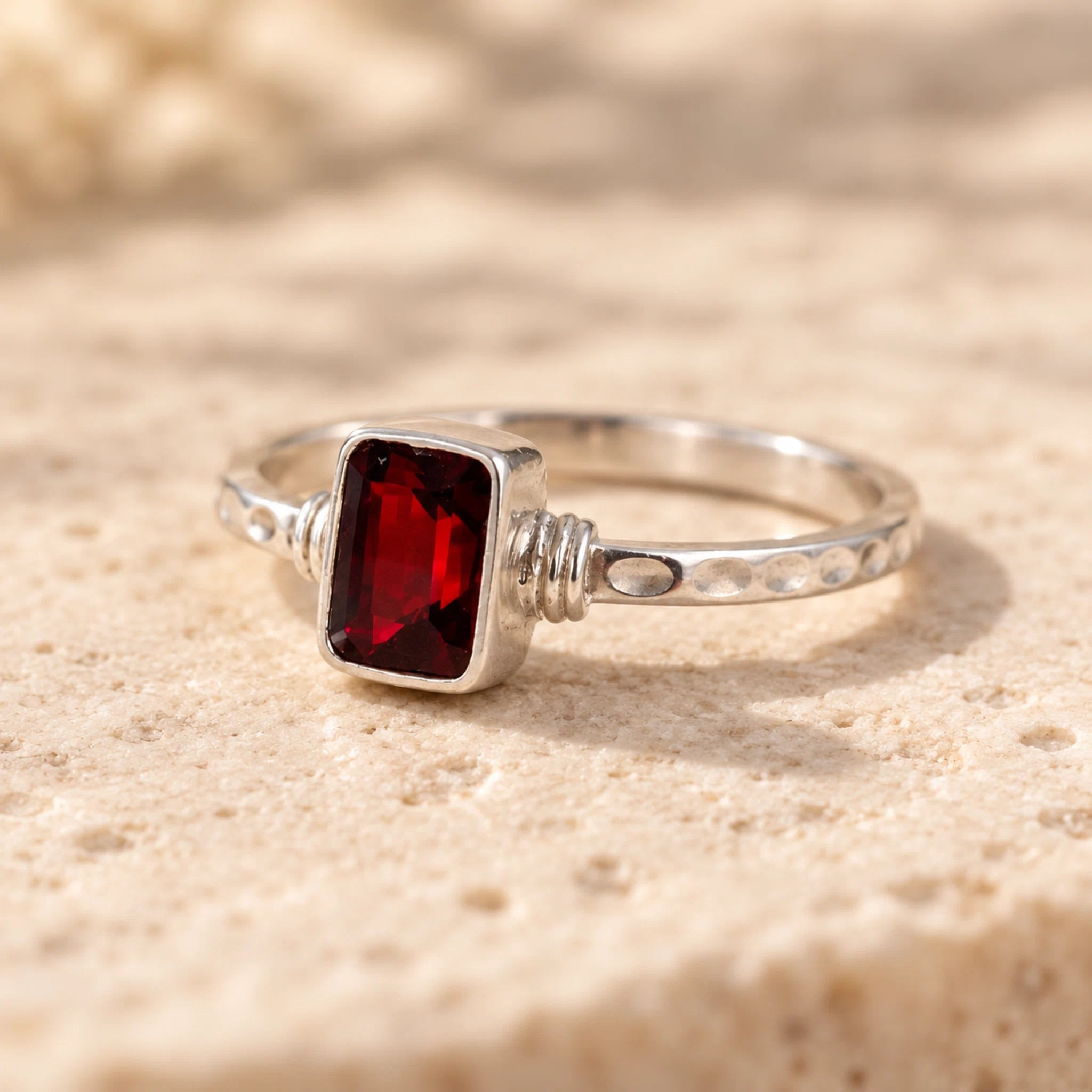 Sterling silver garnet ring with a deep red emerald-cut garnet on a textured beige stone