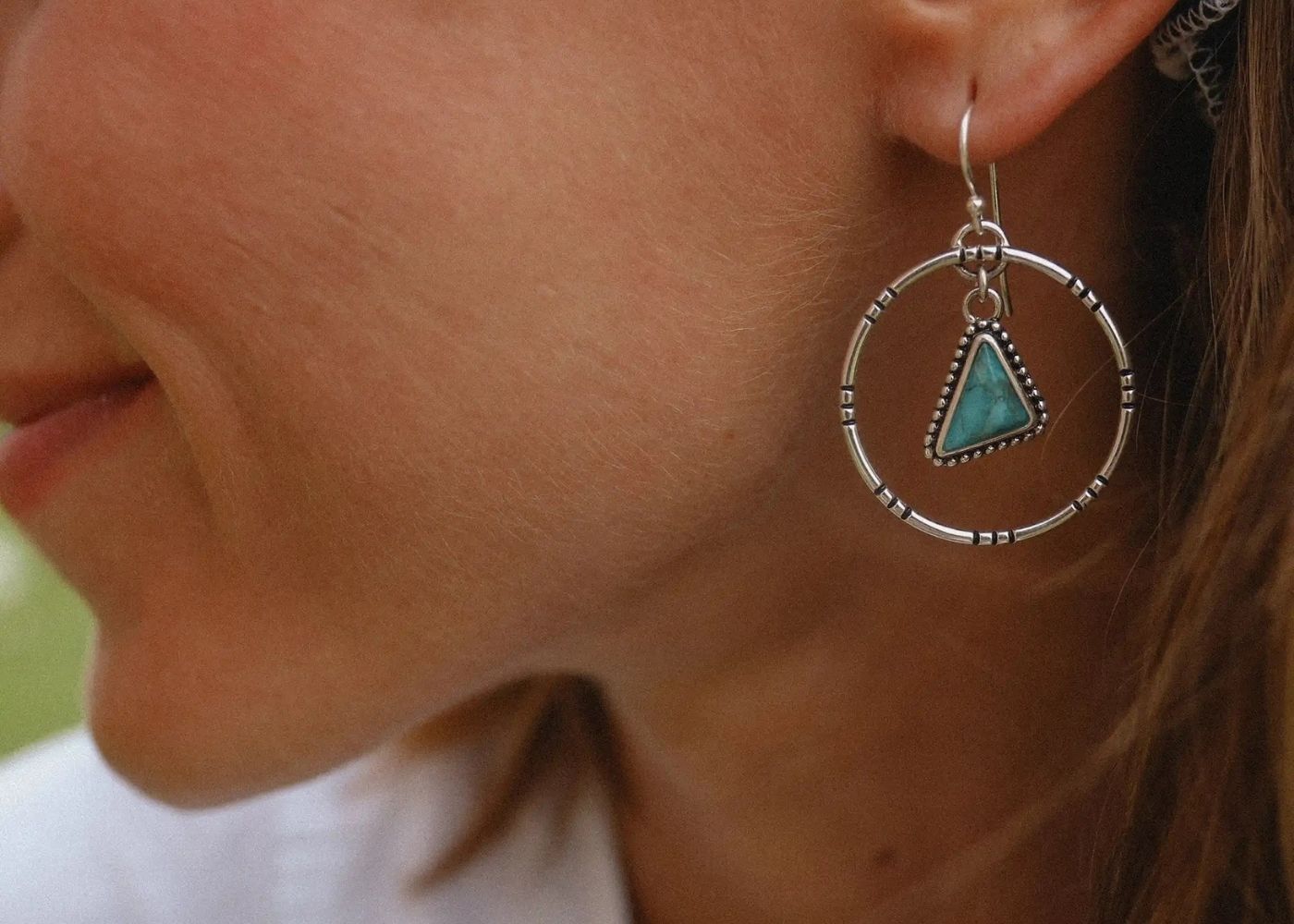 Close-up of a woman wearing a silver earring with a turquoise stone.