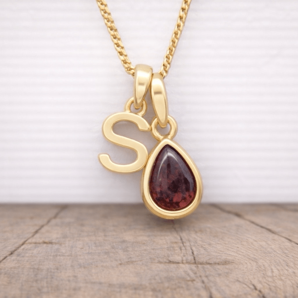 gold s initial and january birthstone garnet necklace hanging above a wooden surface