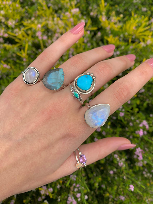 Hand wearing multiple rings with gemstones against a blurred natural background