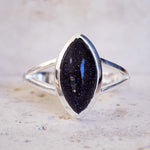 Silver ring with a large black gemstone on a textured surface