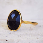 Gold ring with a black gemstone on a light marble background
