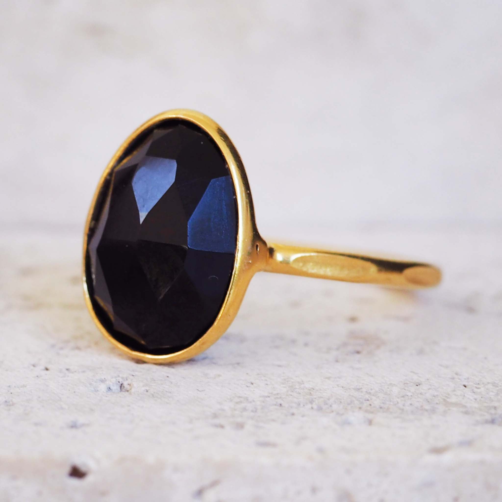 Gold ring with a black gemstone on a light marble background