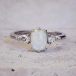 Silver ring with a central opal stone and smaller diamonds on a light background