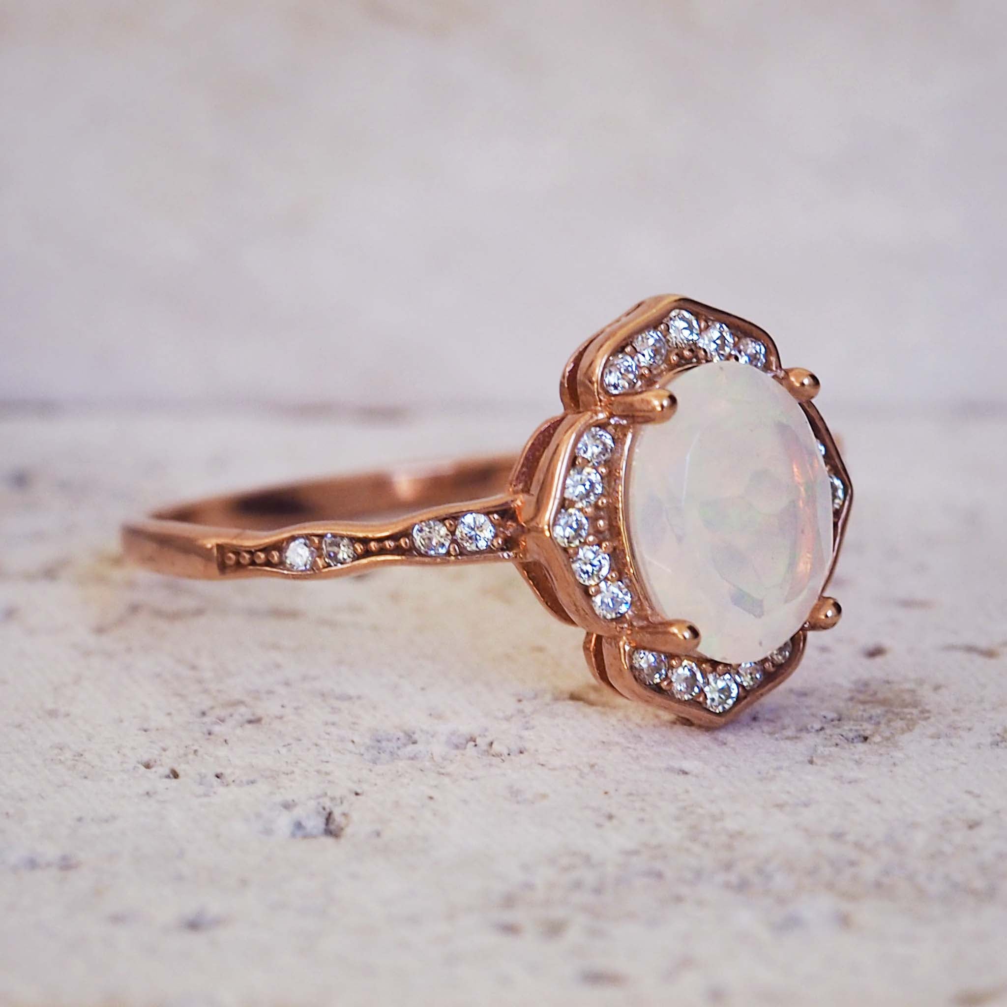 Rose gold ring with a large opal stone and smaller diamonds on a textured surface