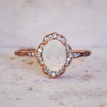 Rose gold ring with an opal stone and diamond accents on a light background