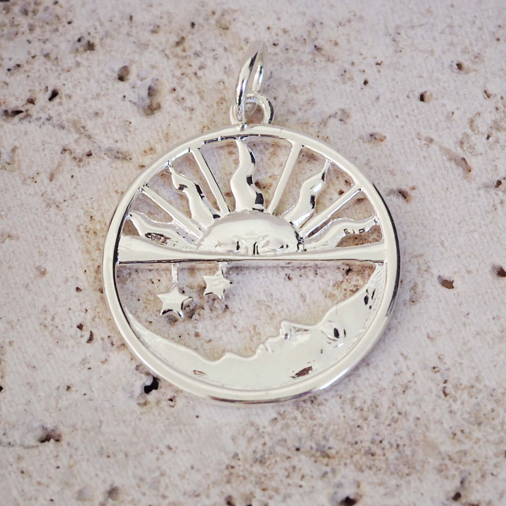 Silver pendant with sun and moon design on a textured surface