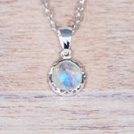 Silver pendant with a rainbow moonstone on a wooden surface