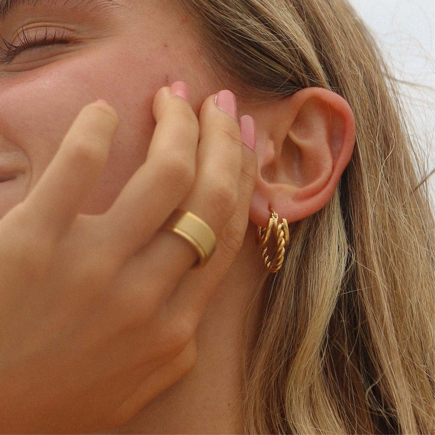 Close-up of a person wearing a gold hoop earring with a blurred background