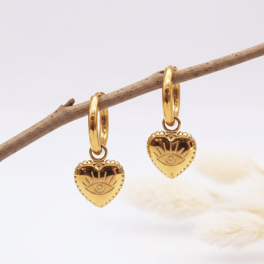 Gold heart-shaped earrings with eye design on a branch against a light background