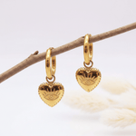 Gold heart-shaped earrings with eye design on a branch against a light background