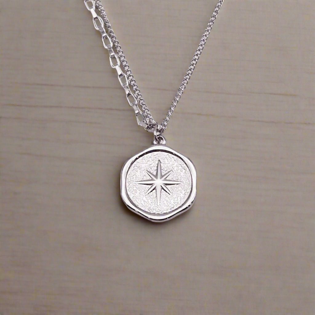Silver necklace with a round pendant featuring a star design on a beige background