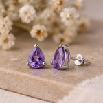 Amethyst stud earrings with butterfly back on beige stone with dried white flowers behind