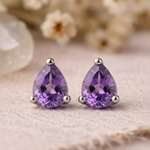 Close-up of faceted pear-shaped amethyst stud earrings in sterling silver claw settings on linen