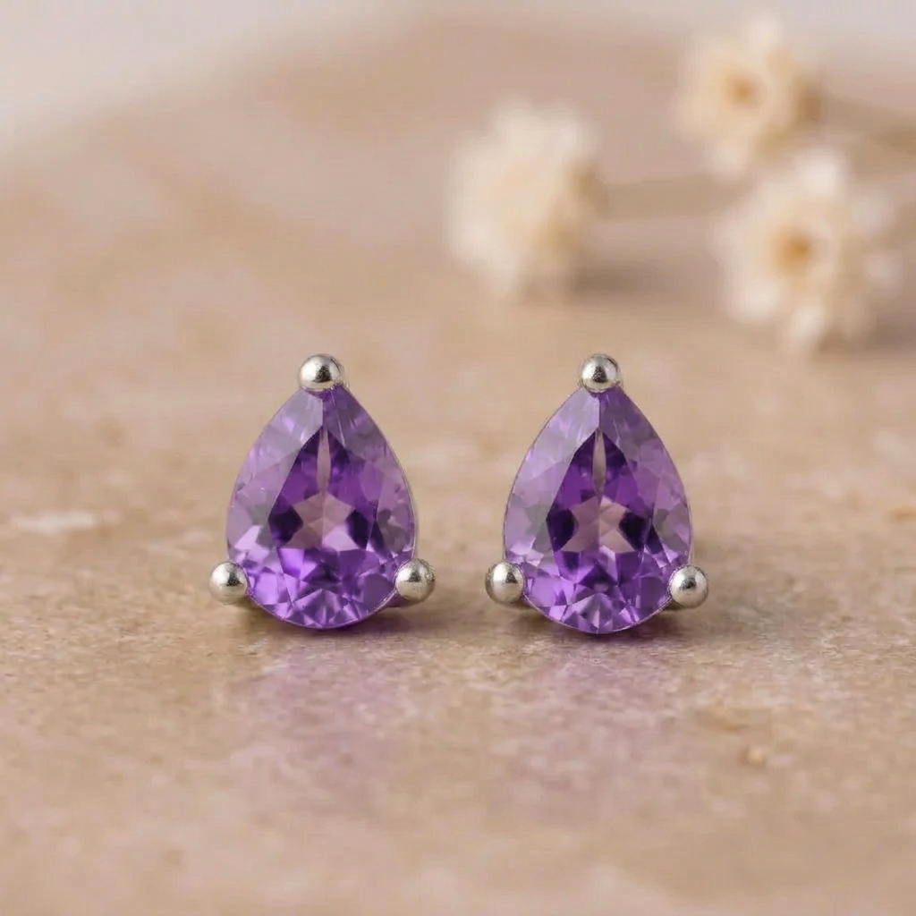 Pair of pear-shaped amethyst stud earrings in sterling silver claws on beige stone with small white flowers