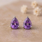 Pair of pear-shaped amethyst stud earrings in sterling silver claws on beige stone with small white flowers