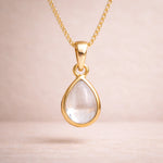 Gold necklace with a teardrop-shaped natural herkimer quartz cabochon pendant on a beige background