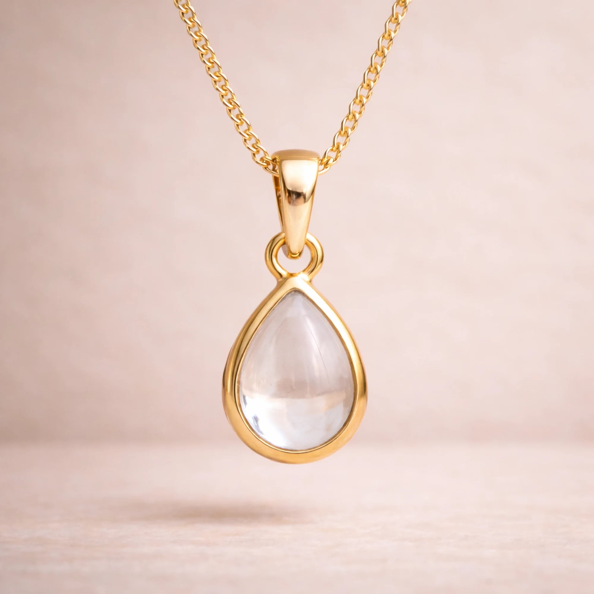 Gold necklace with a teardrop-shaped natural herkimer quartz cabochon pendant on a beige background