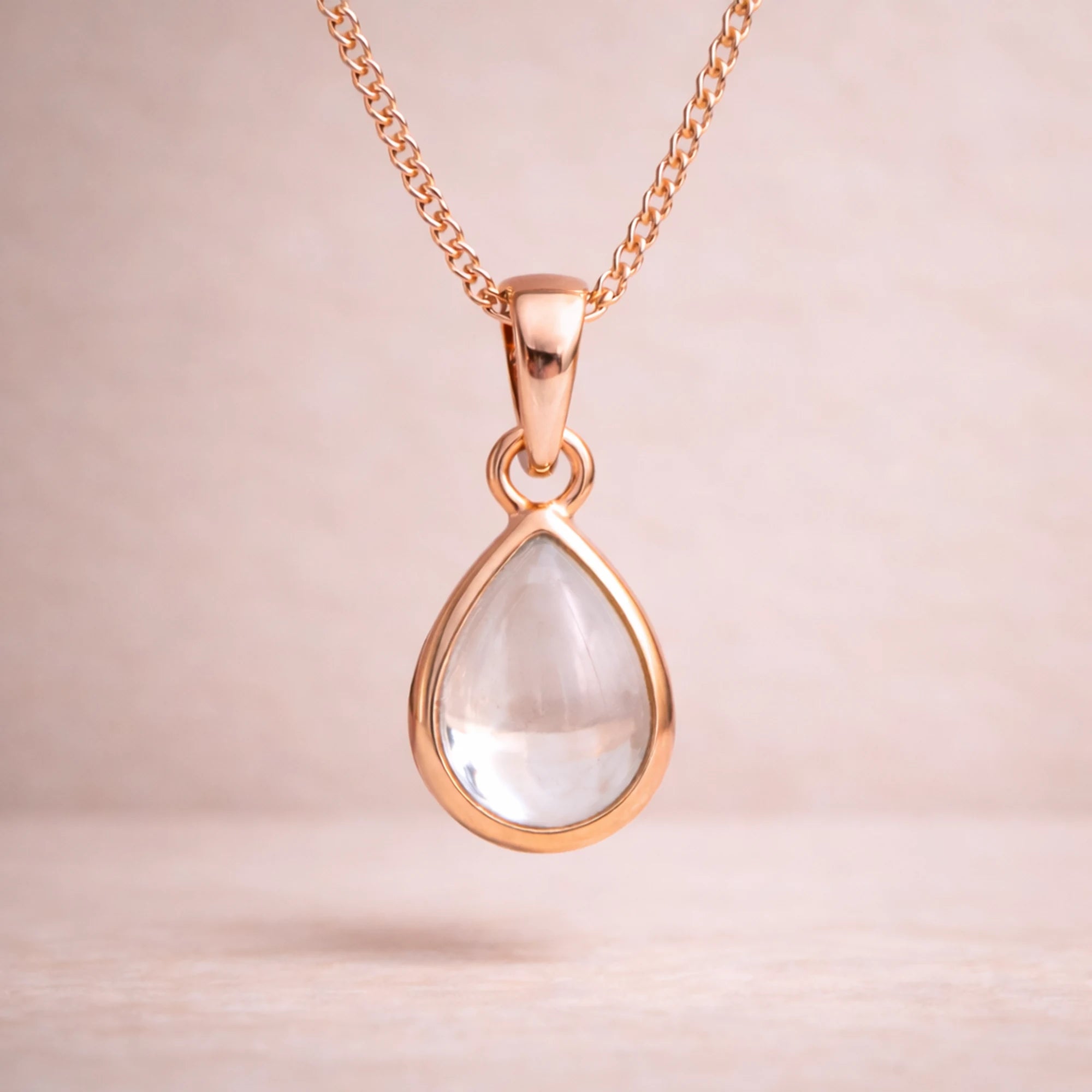 Rose Gold necklace with a teardrop-shaped natural herkimer quartz cabochon pendant on a beige background