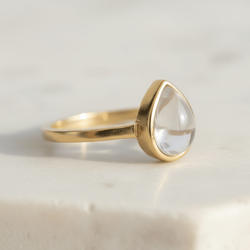 Gold ring with a clear herkimer quartz teardrop-shaped gemstone on a light background