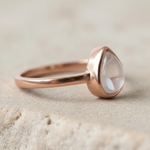 Rose gold ring with a clear herkimer quartz gemstone on a beige background