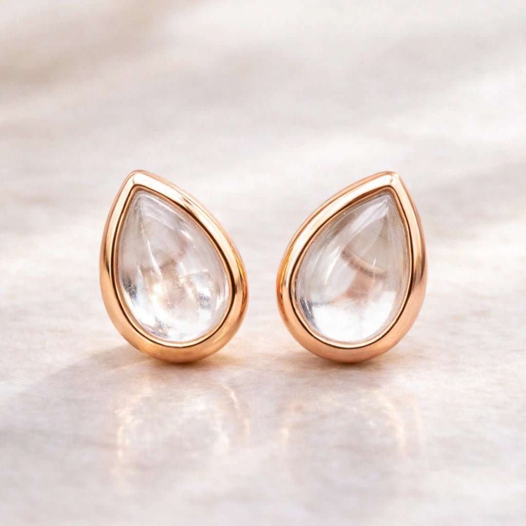 Teardrop-shaped natural herkimer quartz gemstone earrings with rose gold frames on a soft beige background