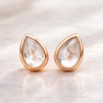 Teardrop-shaped natural herkimer quartz gemstone earrings with rose gold frames on a soft beige background