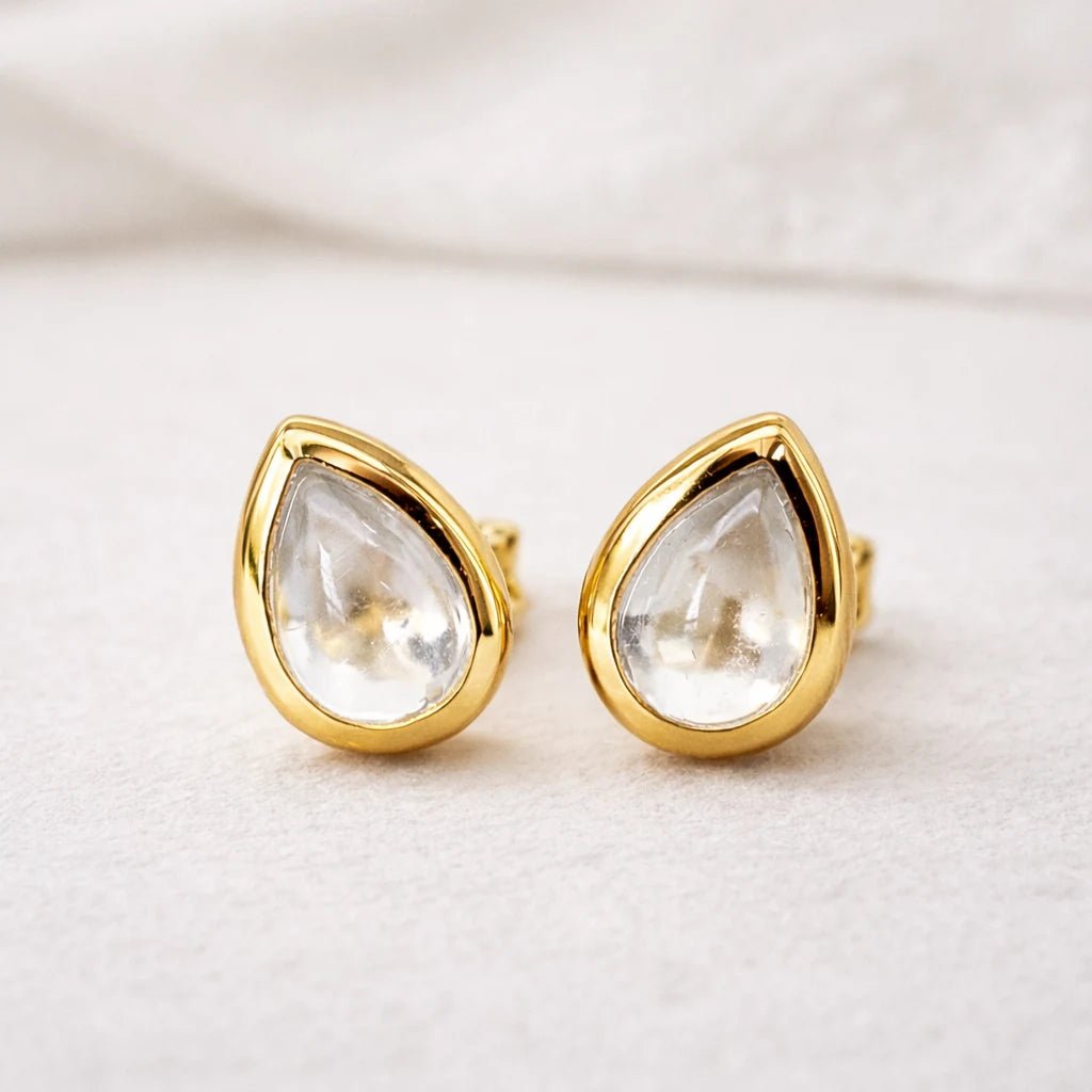 Gold stud earrings with clear natural herkimer quartz teardrop-shaped gemstones on a light background