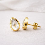 Gold stud earrings with clear herkimer quartz teardrop-shaped stones on a light background