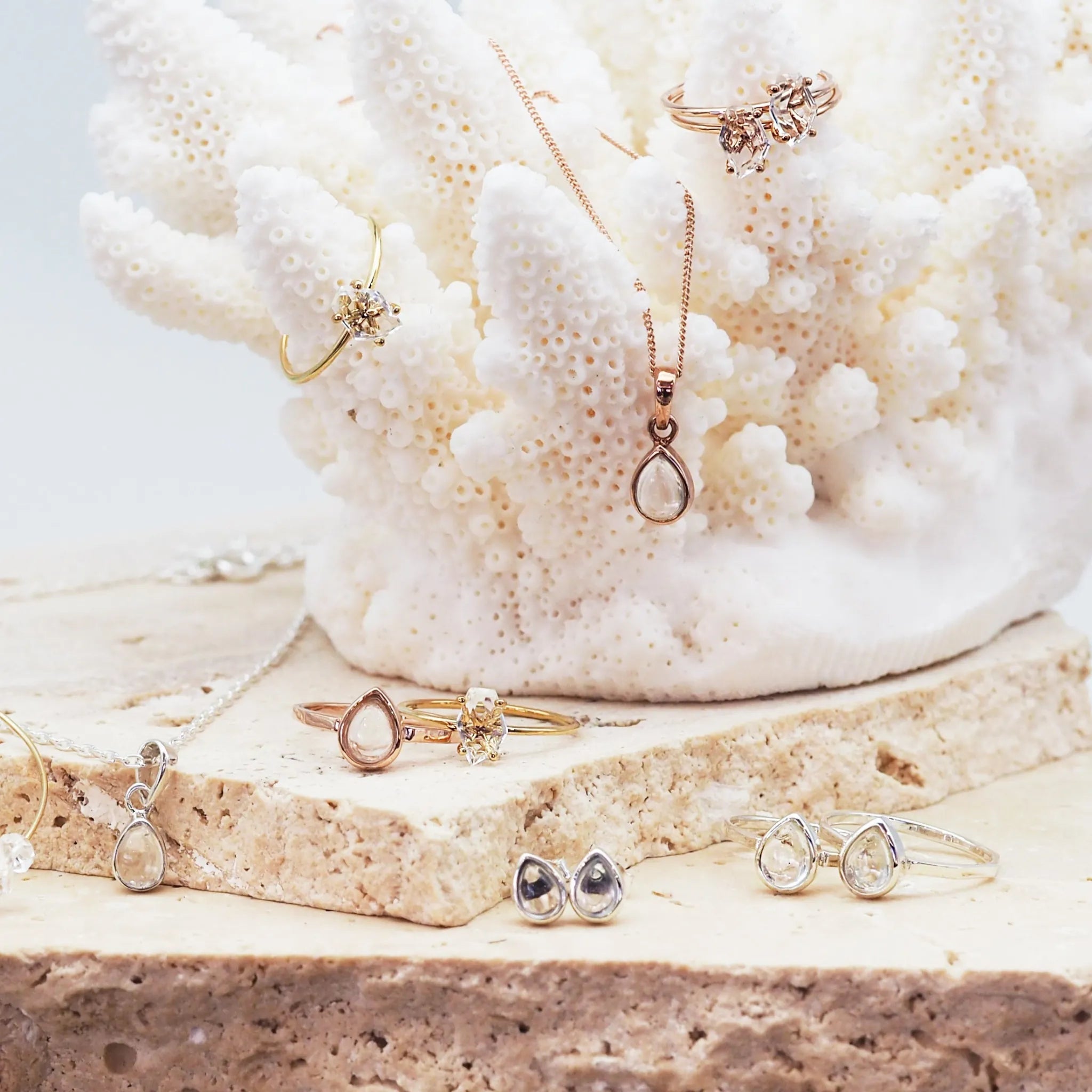 Group shot of april birthstone herkimer quartz Jewelry including rings and necklaces on a coral and stone background