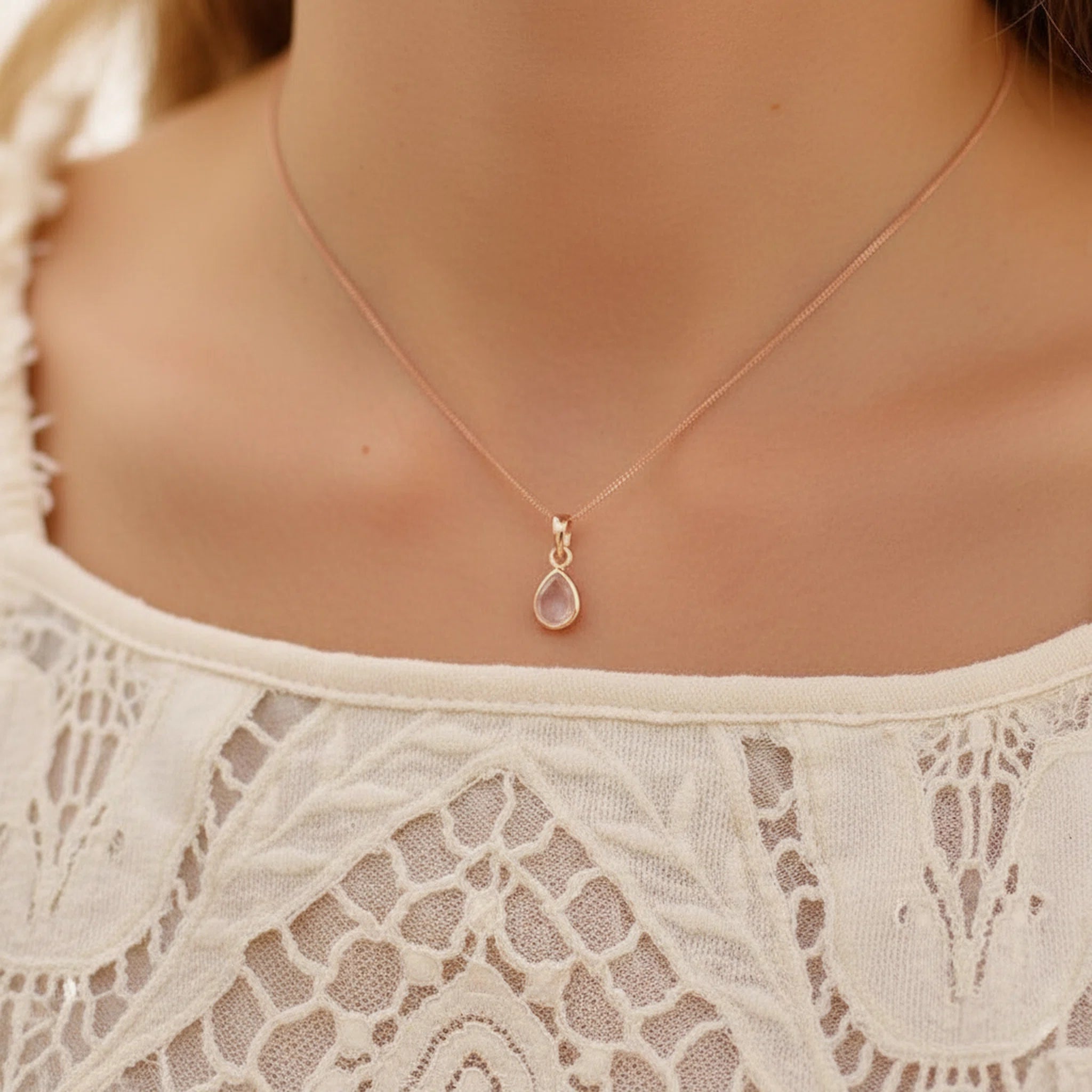 close up of a woman wearing a white lace top and a Rose Gold April Birthstone Necklace with a teardrop-shaped natural Clear Quartz gemstone pendant.