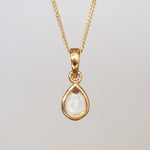 Gold pendant necklace with a clear gemstone on a light gray background