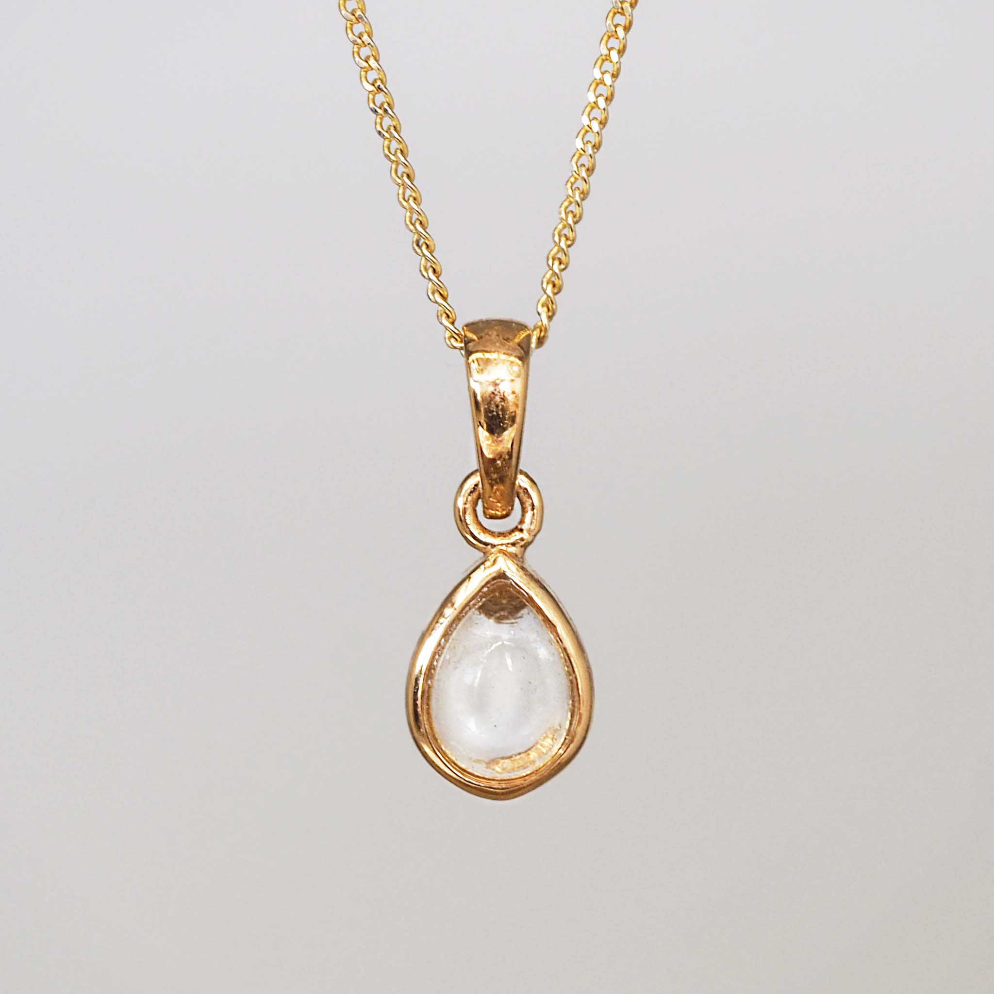 Gold pendant necklace with a clear gemstone on a light gray background