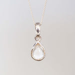 Teardrop-shaped pendant with clear gemstone on a silver chain against a light gray background