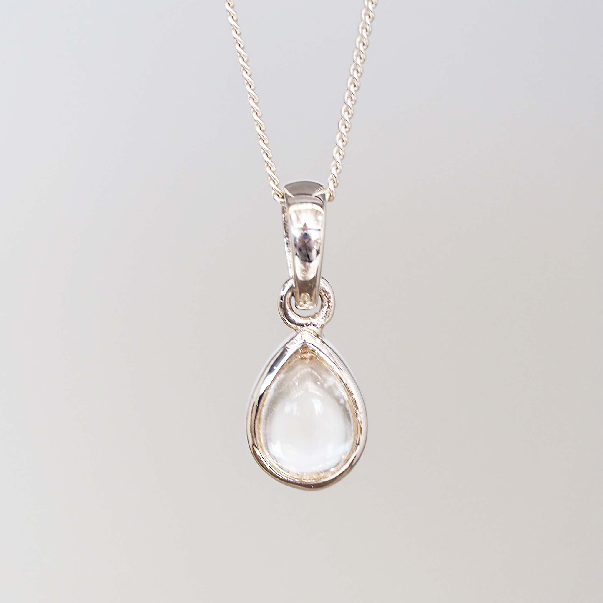 Teardrop-shaped pendant with clear gemstone on a silver chain against a light gray background