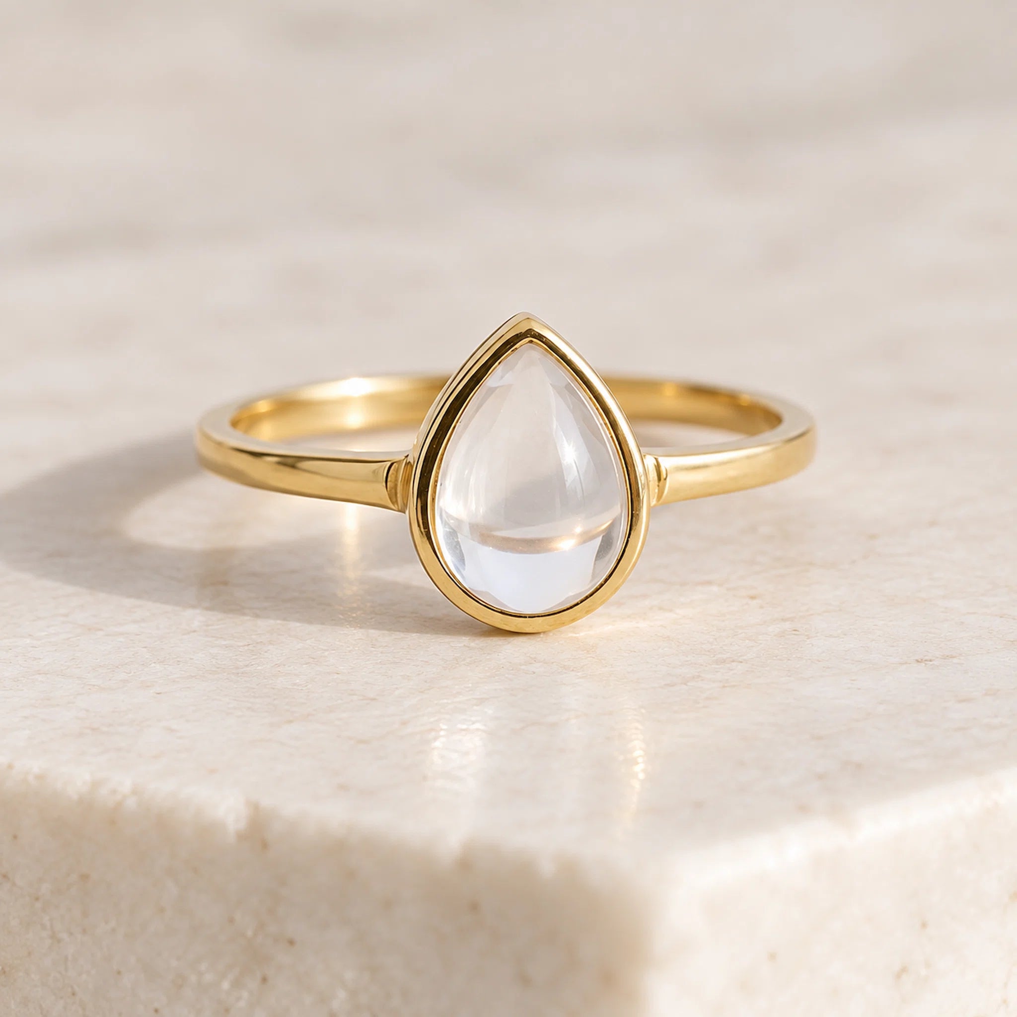 Front view of gold-plated April birthstone ring with pear-shaped clear quartz cabochon in a bezel setting on a light surface