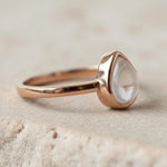 Rose gold April Birthstone ring with a pear-shaped natural clear quartz gemstone on a sandy background