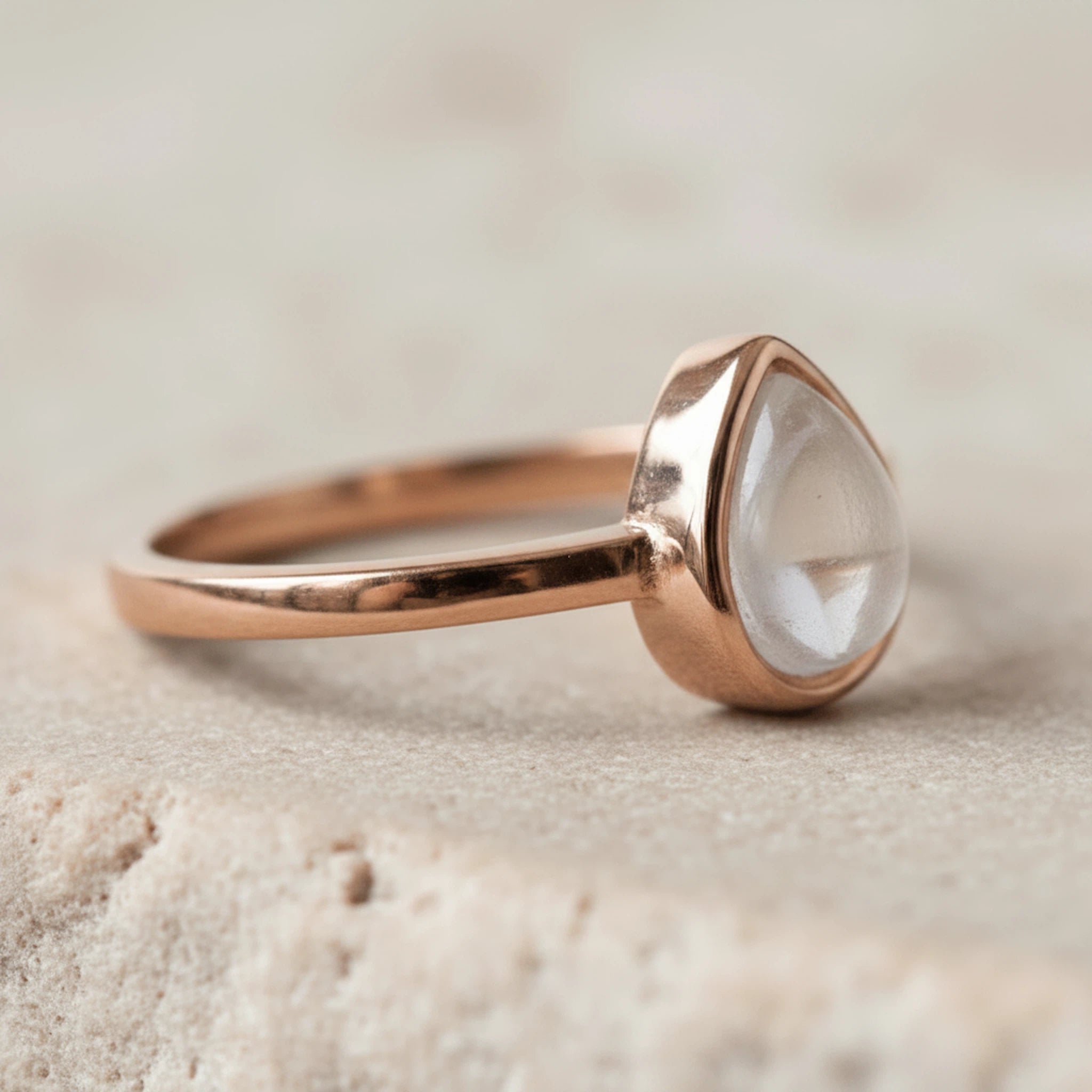 Rose gold April Birthstone ring with a pear-shaped natural clear quartz gemstone on a sandy background