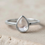 Close up of a Sterling Silver April Birthstone Ring with a teardrop-shaped natural Clear Quartz Gemstone on a light stone surface.