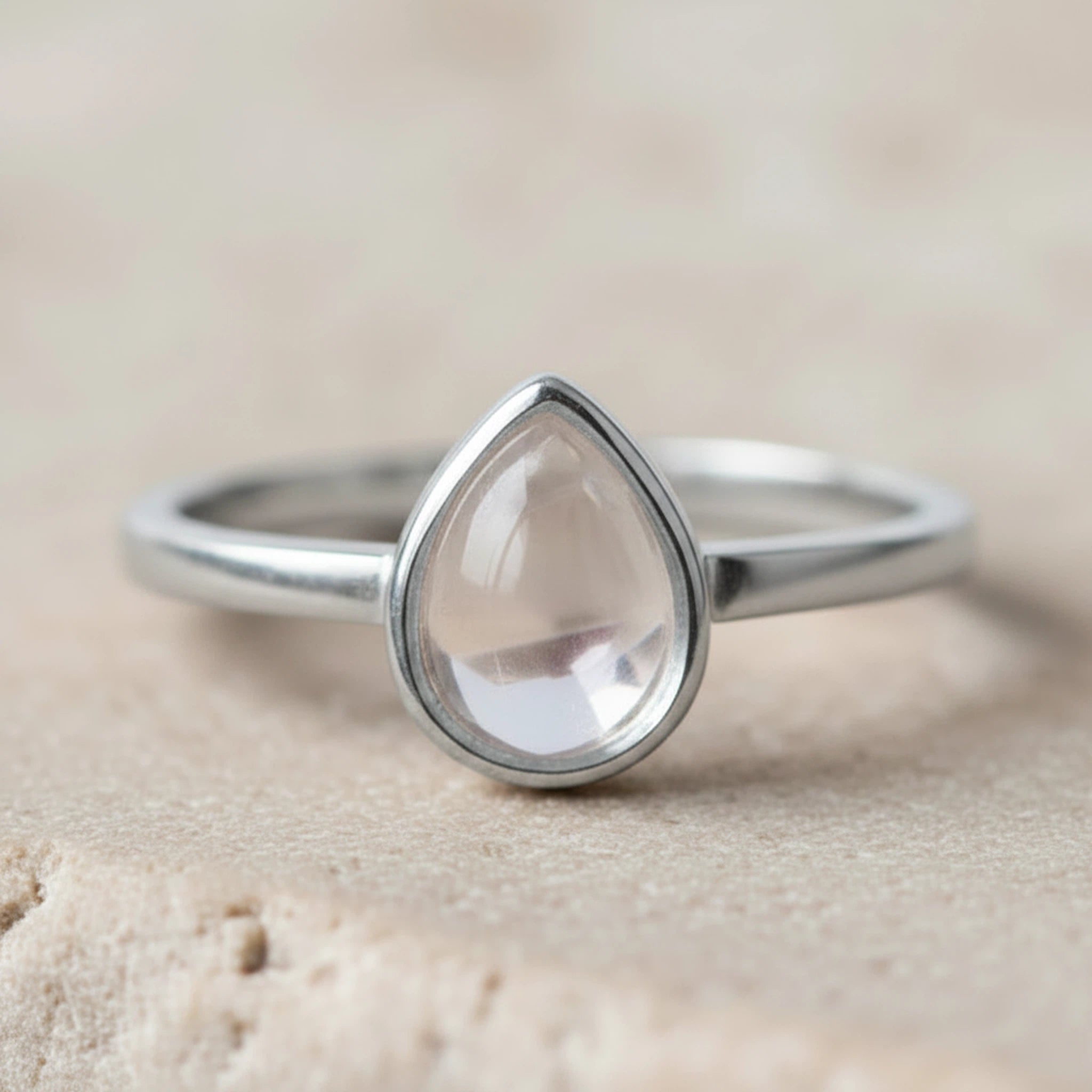 Close up of a Sterling Silver April Birthstone Ring with a teardrop-shaped natural Clear Quartz Gemstone on a light stone surface.