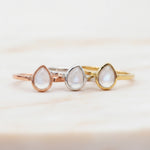 Group shot of three April Birthstone Rings with teardrop-shaped natural Clear Quartz gemstones in rose gold, silver, and gold on a white background.