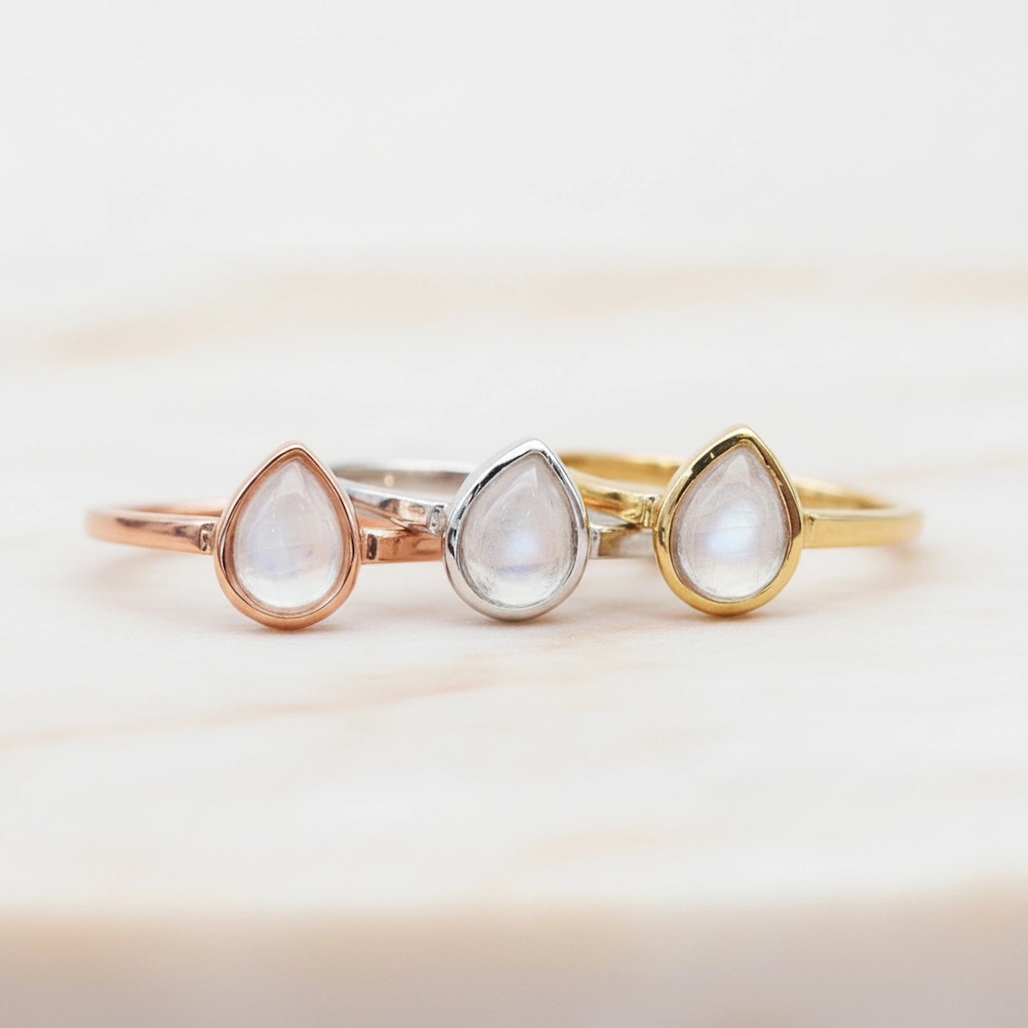 Group shot of three April Birthstone Rings with teardrop-shaped natural Clear Quartz gemstones in rose gold, silver, and gold on a white background.