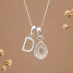 sterling silver initial d april birthstone natural clear quartz pendant necklace against a dark warm beige background