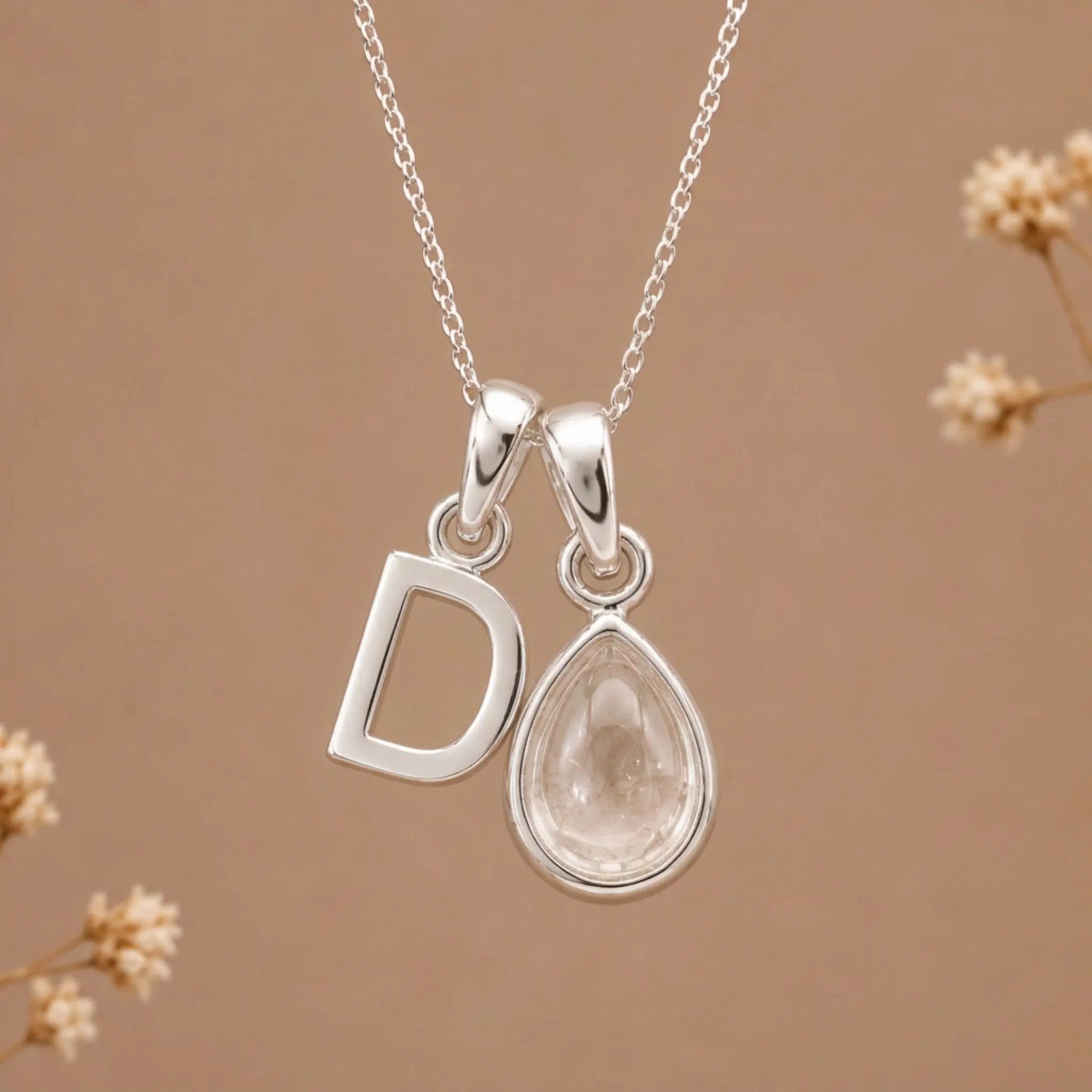 sterling silver initial d april birthstone natural clear quartz pendant necklace against a dark warm beige background