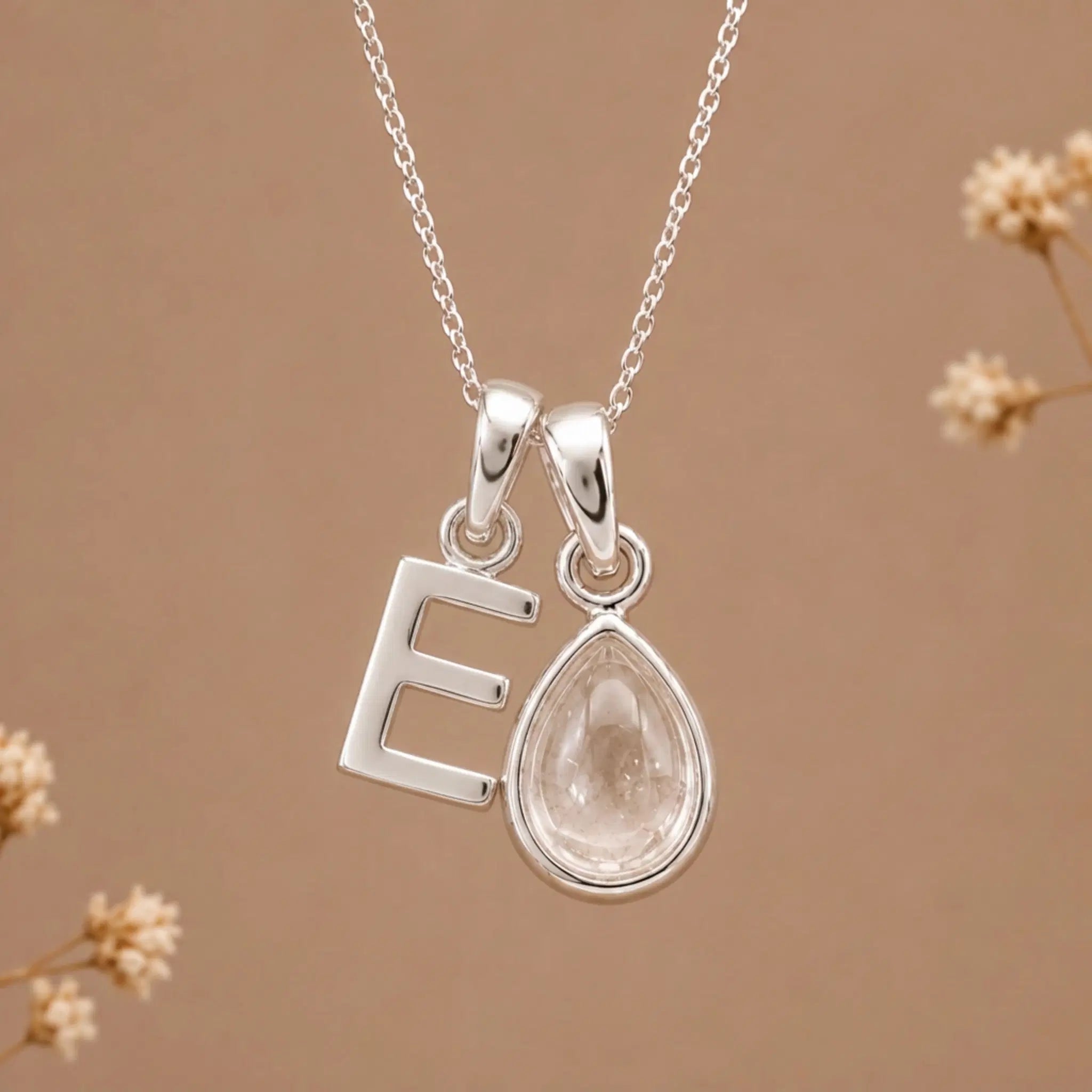 sterling silver initial e april birthstone natural clear quartz pendant necklace against a dark warm beige background
